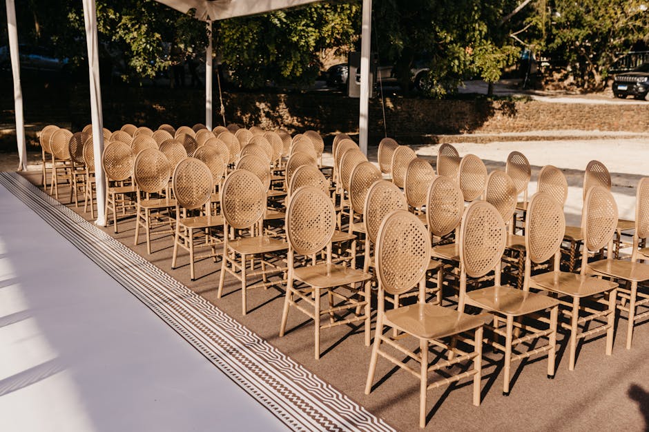 Rows of stylish woven chairs arranged for an outdoor wedding ceremony under a tent.