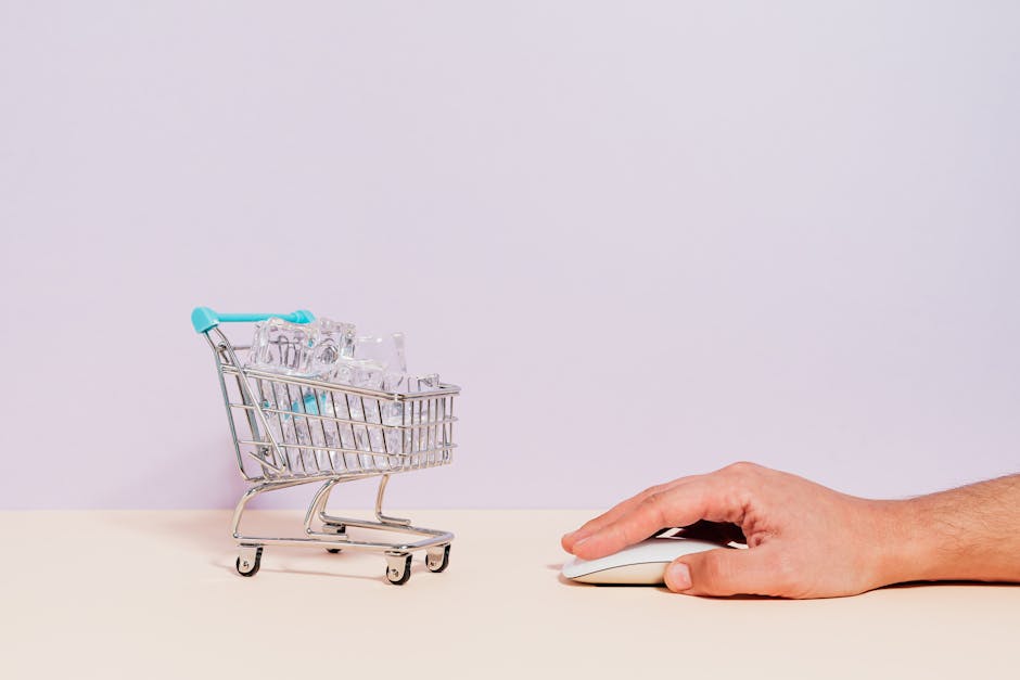 Conceptual image of a hand on a mouse next to a miniature shopping cart filled with ice cubes, symbolizing online shopping.